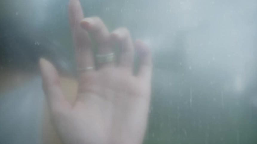 A blurred misty close up of a womans face as seen through the fogged up glass of a shower cabin