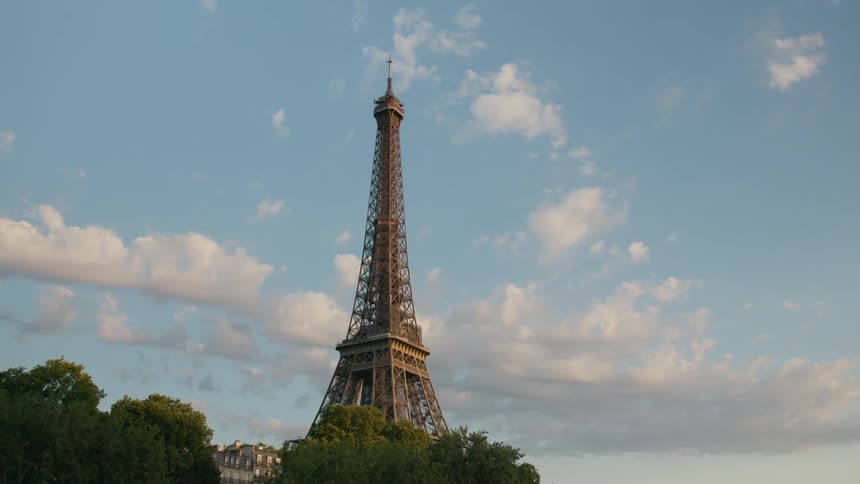 The iconic eiffel tower stretches towards the sky its intricate latticework gleaming against a backdrop of fluffy white clouds