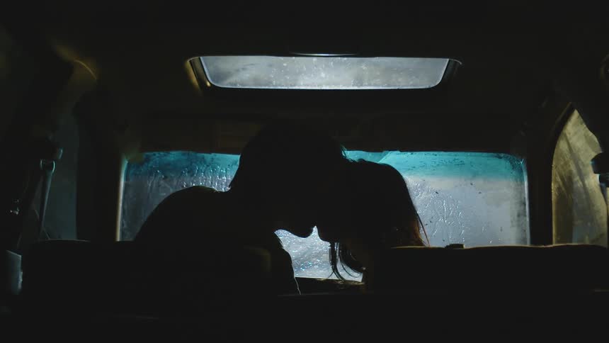 Silhouette of a man and a woman inside a car kissing