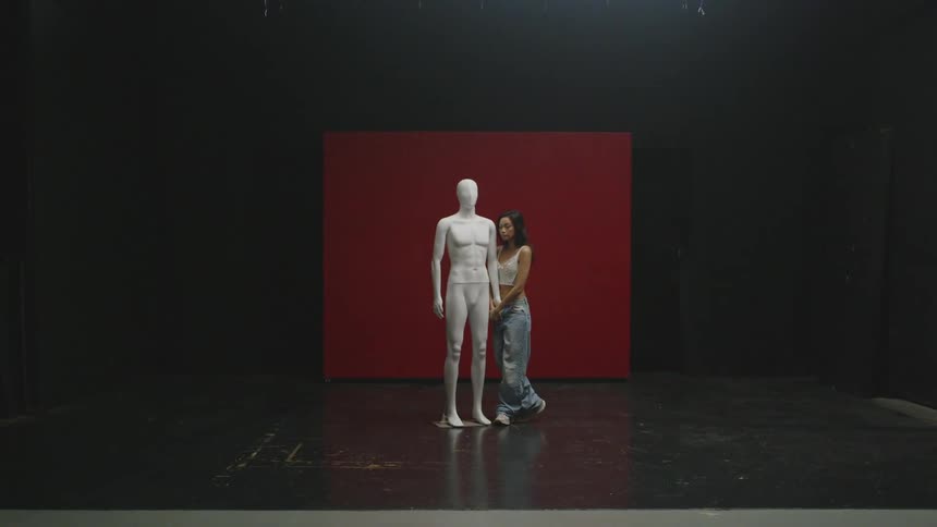 A woman walks over to a mannequin on stage and holds its hand