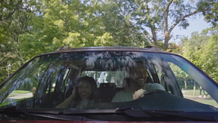 A happy couple driving a red car on a treelined street through a neighborhoodtion