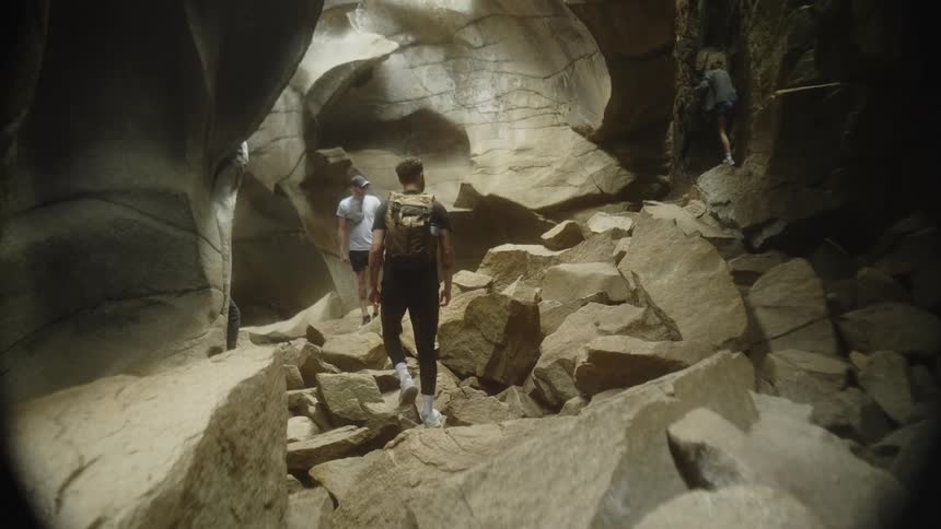 Three people are seen navigating a rocky cave with two walking on a path and one climbing a rock face