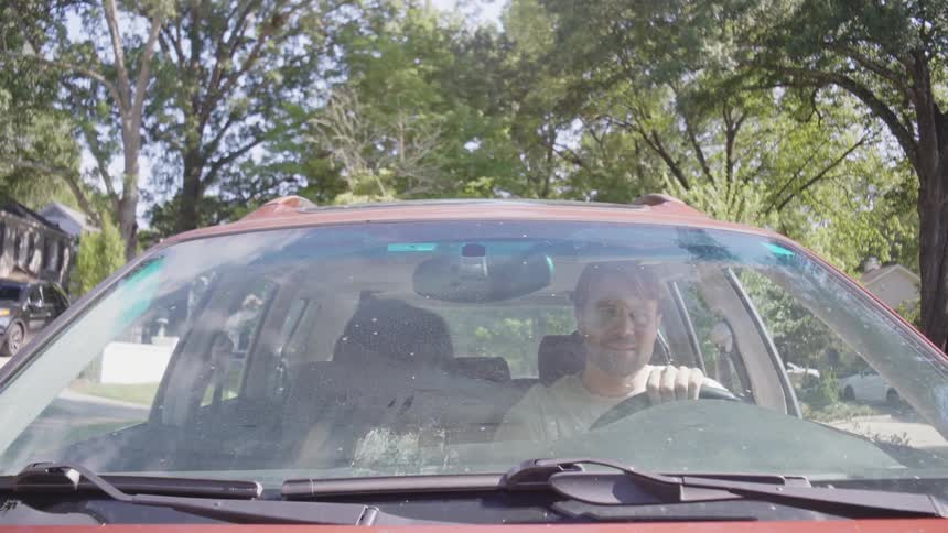 A couple is seen from the front in their car as they are talking and driving down a street