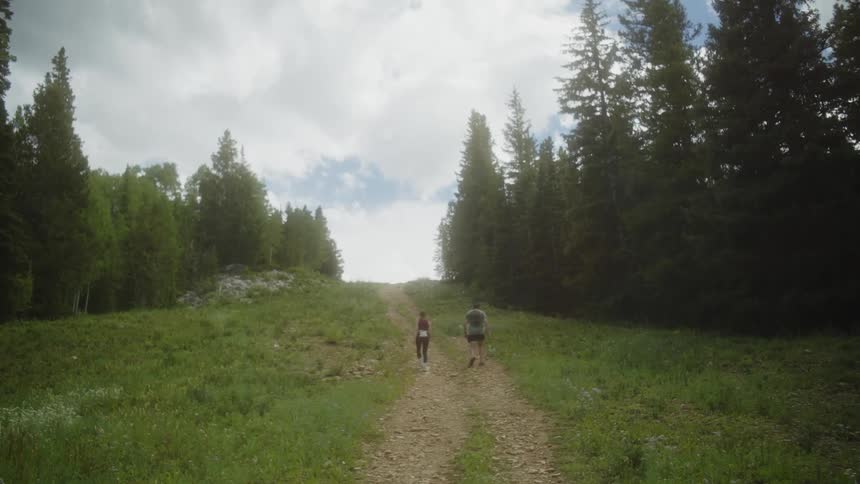 Two teenagers walking on a dirt road between the forest