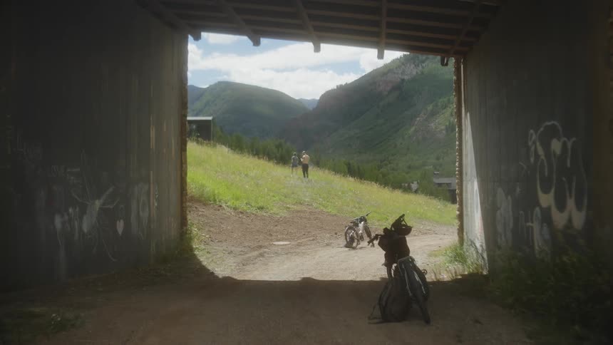 Two bicycles and a trail with a person walking in the background in a natural setting with mountains