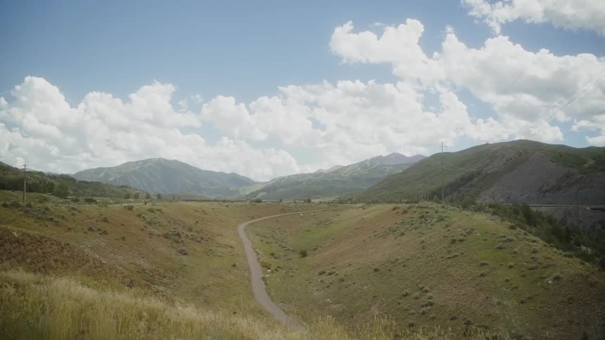 Rural road through a mountain valley with mountains in the distance under a cloudy sky