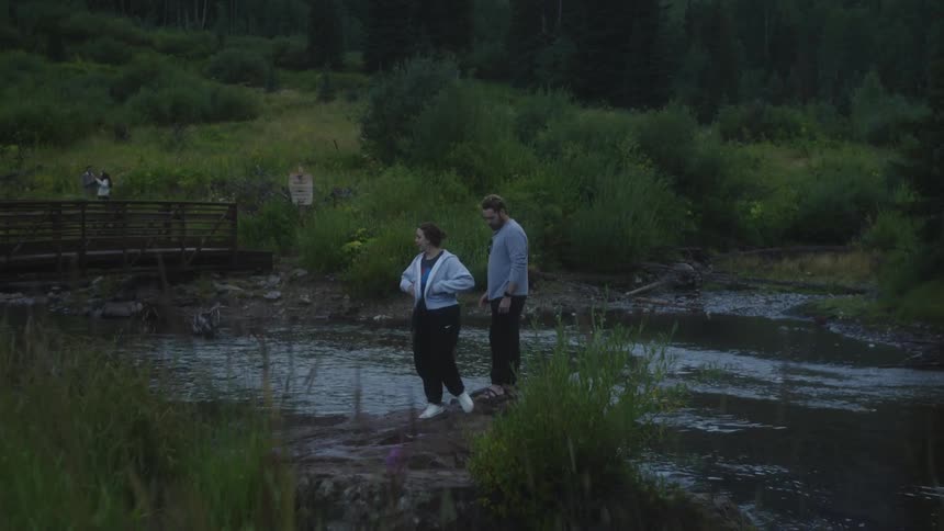 One couple talks while standing on the riverbank while another stands on the bridge on a misty day