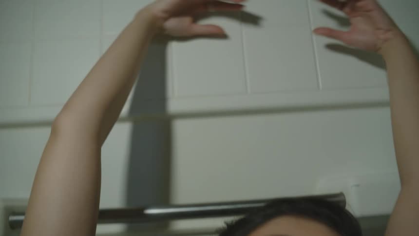 Woman running her hands through her hair and raising her hands up against a white wall
