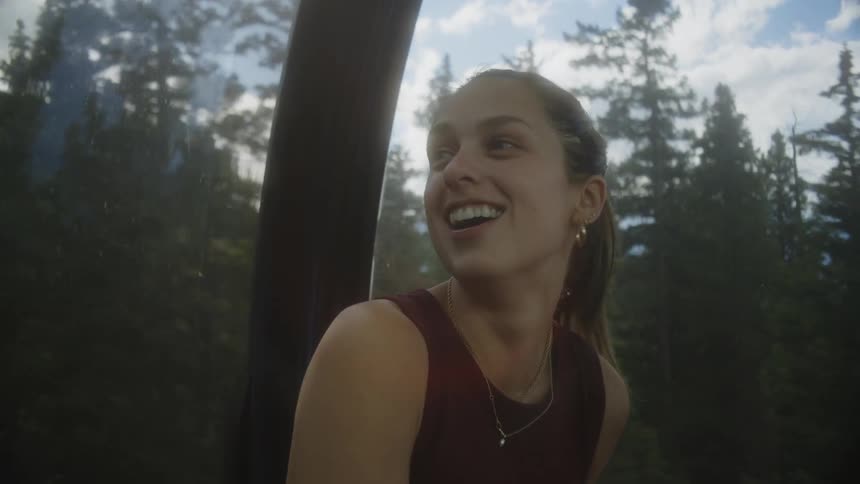 Happy woman talking while riding a cable car through a natural environment surrounded by conifers