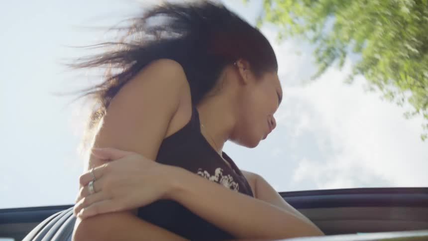 An asian woman is hanging out of the window of a moving vehicle as her long hair blows in the wind