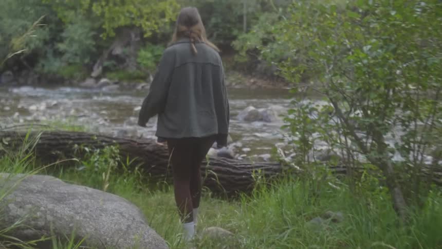 A woman steps on top of a log by the stream