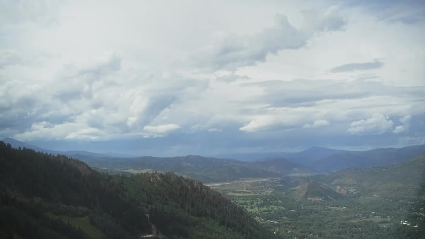 A camera overlooks a hilly valley covered in vegetation