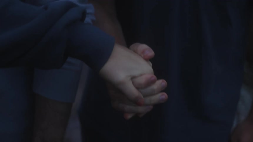 Two individuals holding hands against a dimly lit background