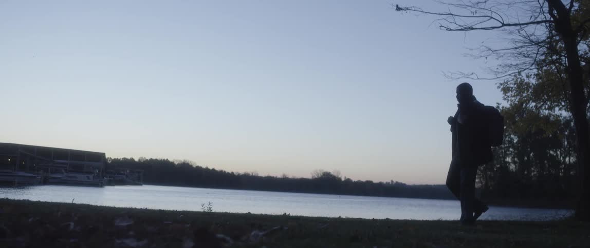A silhouette of a man walks by the lakeside at dusk