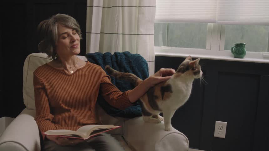 Woman sitting in a chair with a book in her lap as she pets her cat