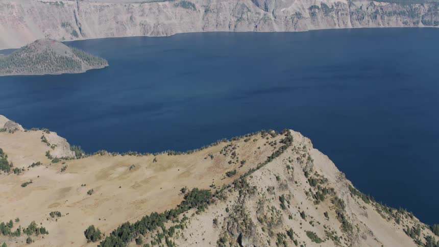 Aerial view of a deep lake with dark blue waters surrounded by steep slopes and sparse vegetation