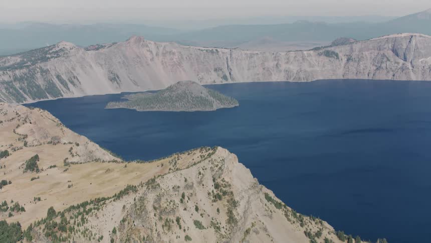 Island sits on blue water surrounded by a mountainous coast on a foggy day