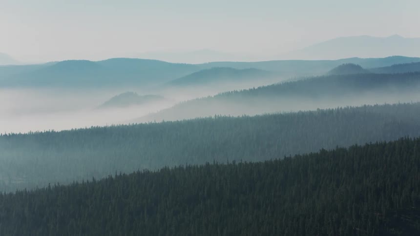 Layers of rolling hills and dense forests stretch into the distance shrouded in a soft ethereal mist
