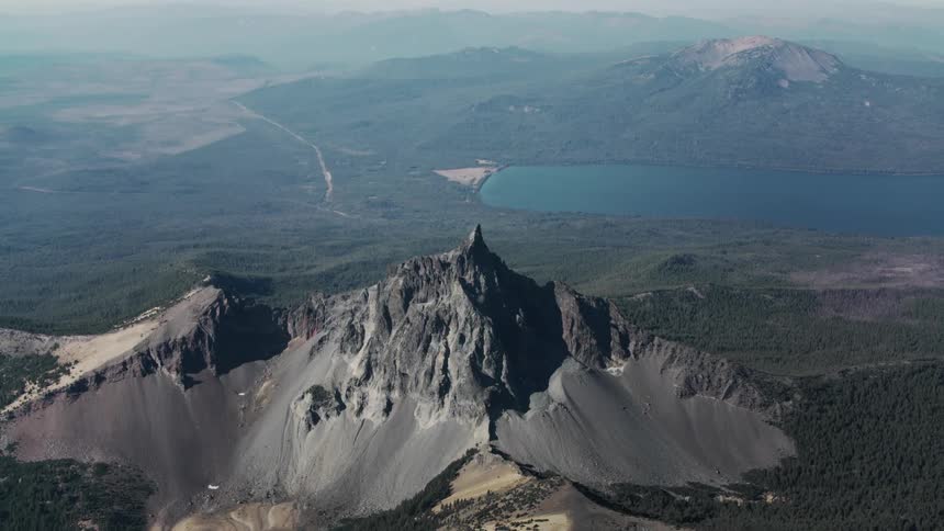 A sharp rocky peak rises dramatically above a vast landscape of rolling hills and distant mountains
