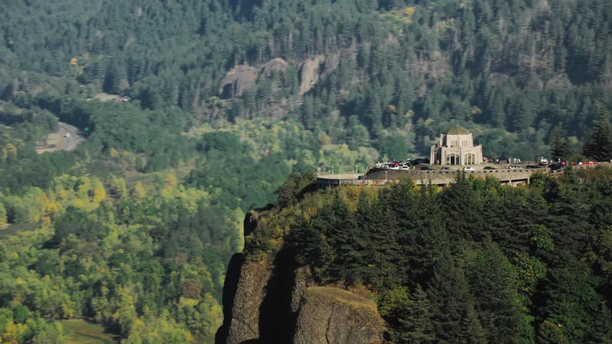 An aerial view of a building on top of a tall mountain and below there is a landscape of a region with many forests