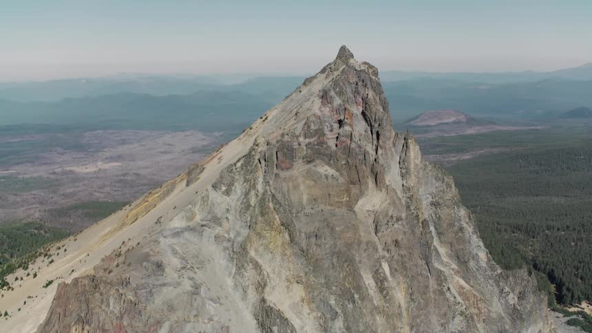 A sharp rocky peak rises dramatically above a vast landscape of rolling hills and distant mountains