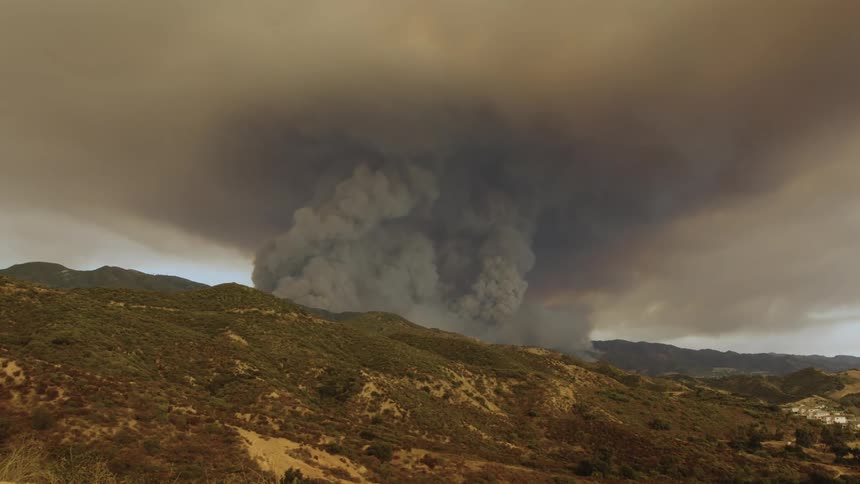 Dark smoke rises over a mountain and fills the air