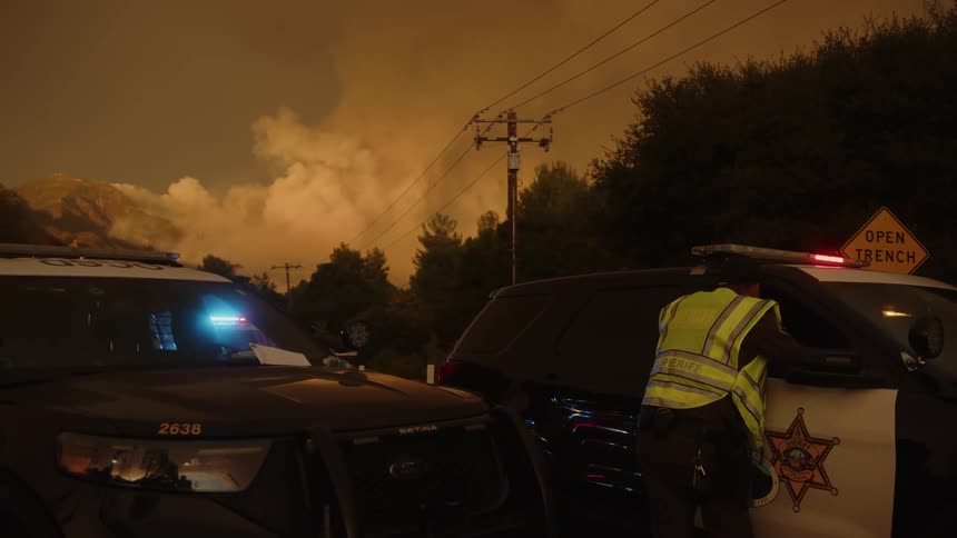 Orange sky and shrouded in smoke police and vehicles are operating on a road