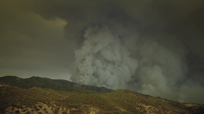 Thick dark smoke rises over the mountain and fills the air