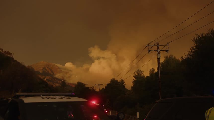 A volcano has erupted and releasing a lot of smoke into the sky and there are some police cars parked with their emergency lights on