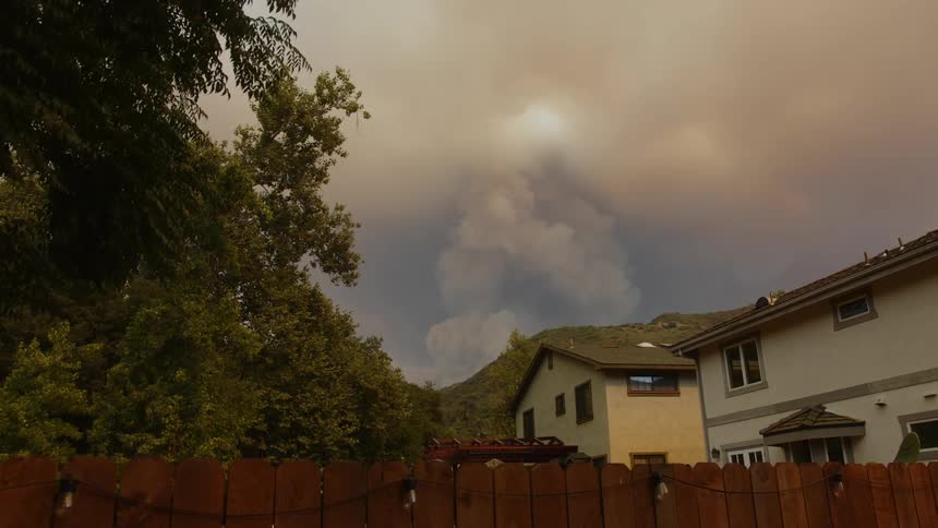 Smoke rises over a mountain behind a house