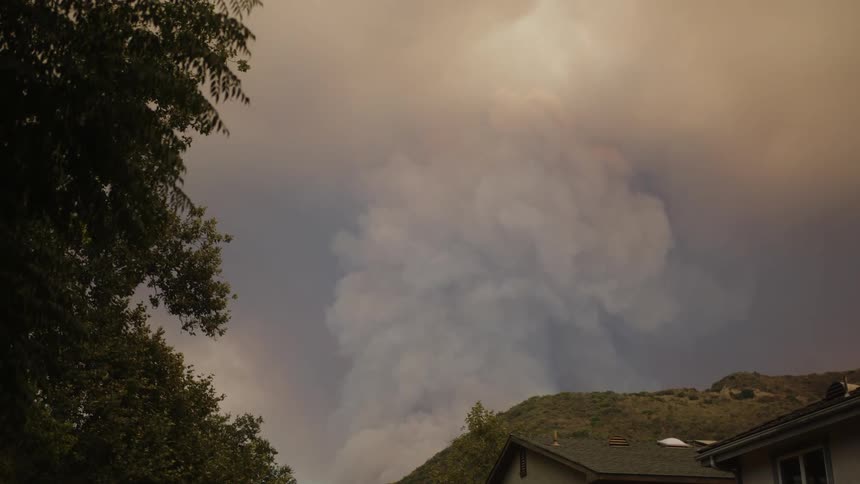 Smoke rises over a mountain behind a house