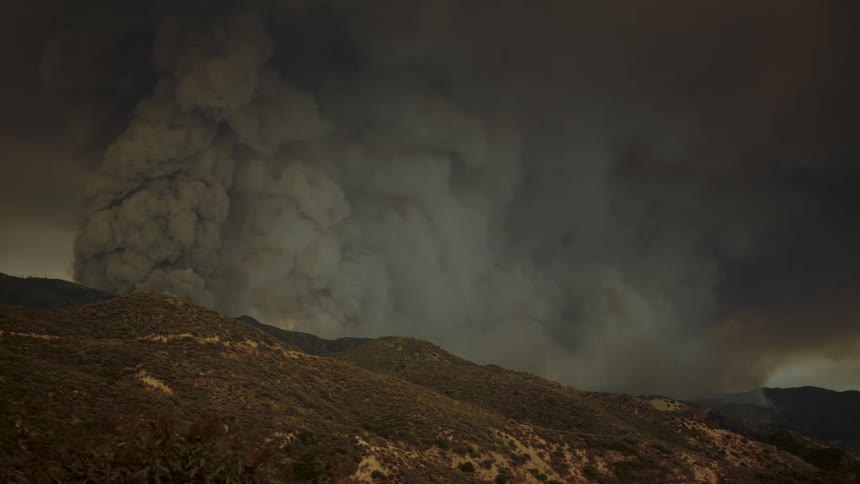 Thick dark smoke rises over the mountain and fills the air