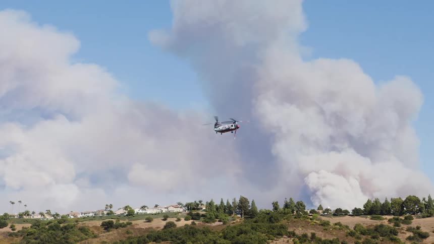 Rescue helicopter flying over a natural area with smoke in the background