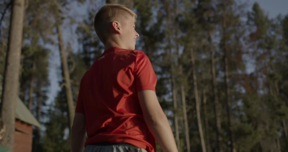 Boy in a red shirt throwing something outdoors while another boy in green is beside him