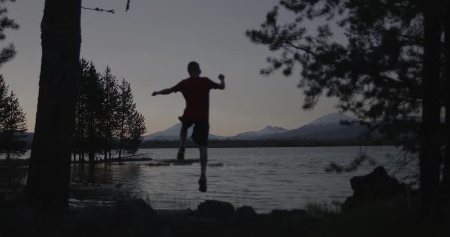 A boy jumping at the edge of a lake