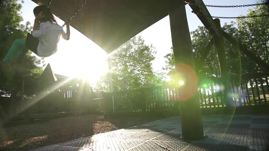 Two young children swinging on a playground at sunset