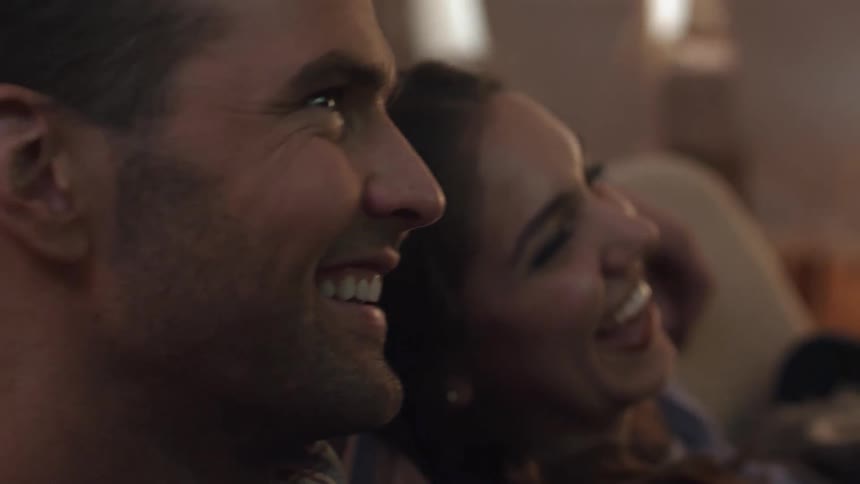 A man and woman smile and laugh sitting on a couch