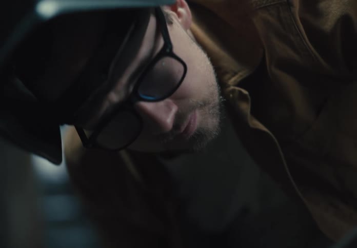 A person wearing glasses and a welding helmet is leaning forward focused on a task