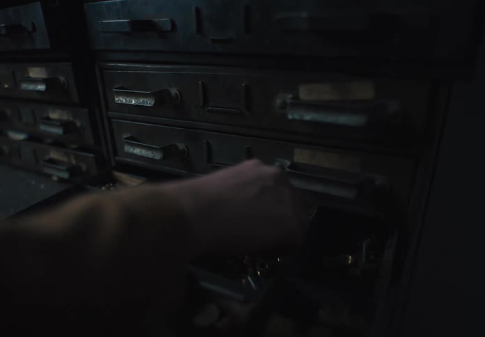 A person opens a drawer in a row of metal filing cabinets revealing compartments filled with small tools