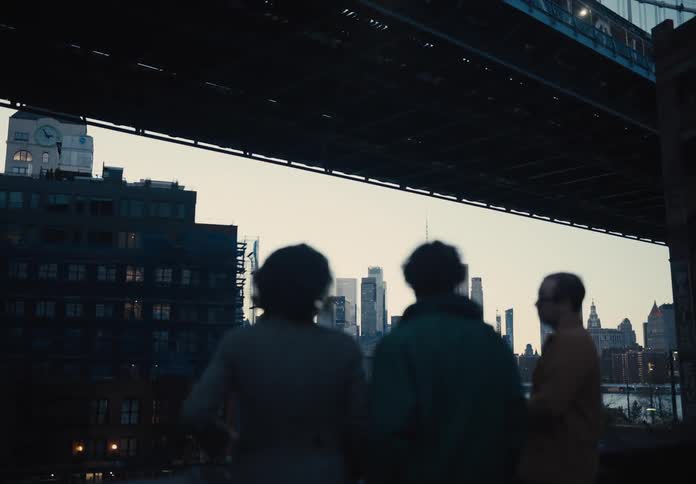 Three people with a panoramic view of a metropolis talking below a bridge