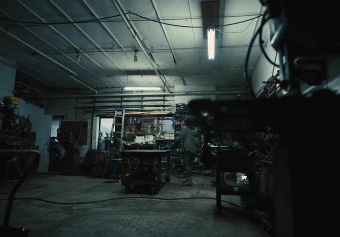 Man walks to the rolling workbench in the center of his workshop and continues a project