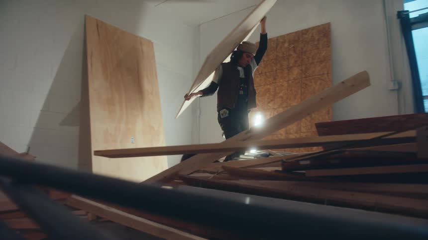 Man picking up a wooden board and walking towards a table in a room