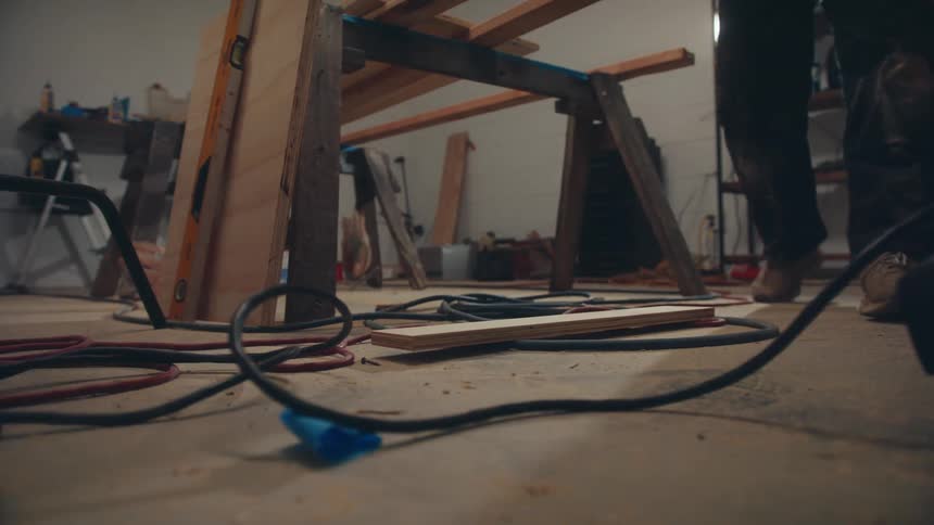 Carpenter picking up a piece of wood from the floor of a garage