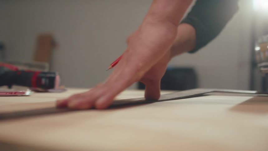 Young man with a pencil and a ruler measuring a wooden board