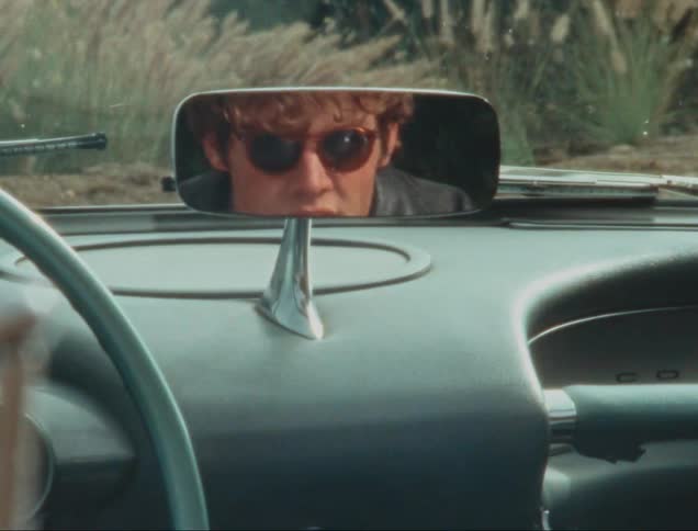 Man wearing glasses reflected in the rearview mirror of a classic car
