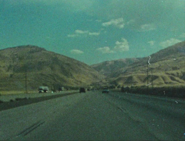 A highway winds through a barren mountainous landscape under a bright blue sky