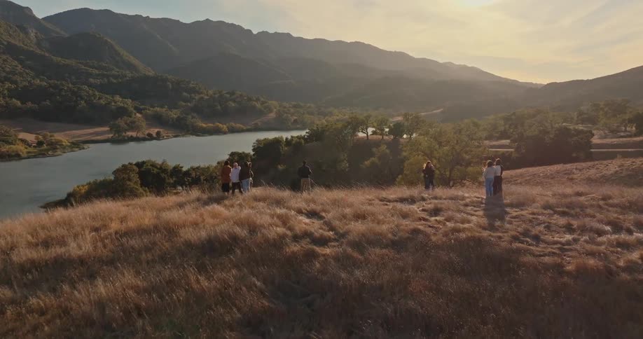 Aerial view of groups of people on a hill with a sea and mountains in the background