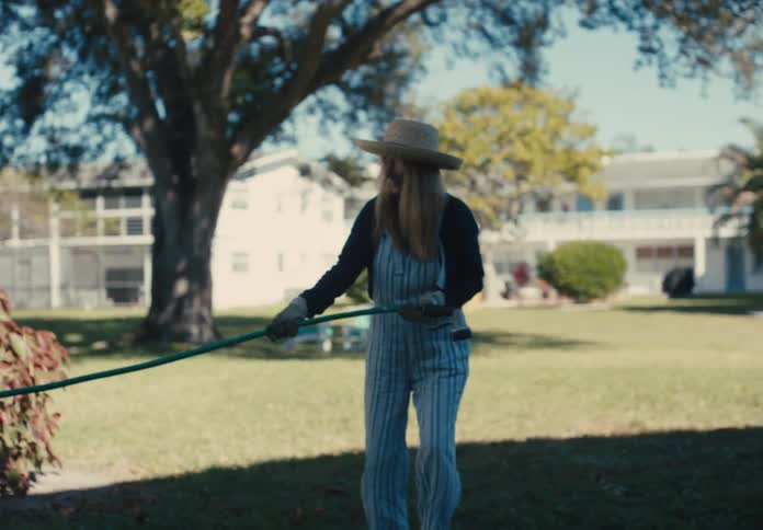 Woman with hat pulling a hose in a garden