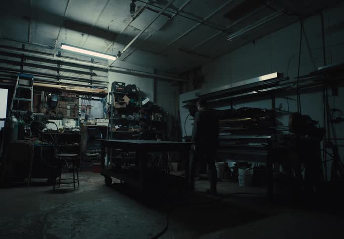 Man walks across a workshop and bends to turn off the electric lights