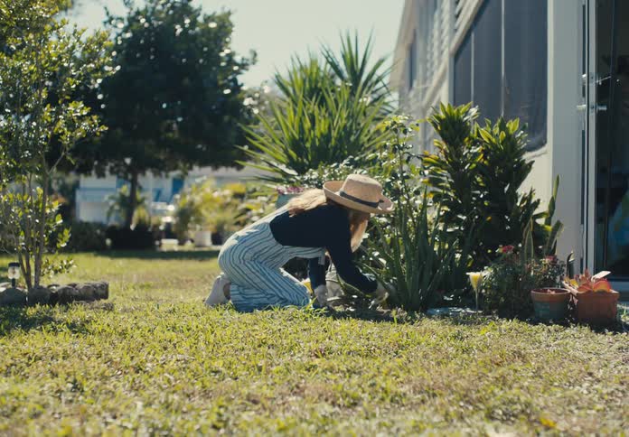 Woman with sun hat crouching gardening with plants